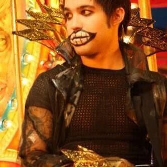 an image of pete wentz as mr sandman in the music video for 'america's suitehearts' by fall out boy. he has short dark hair and a second set of teeth painted over his lips. he looks off to the side with a neutral expression.